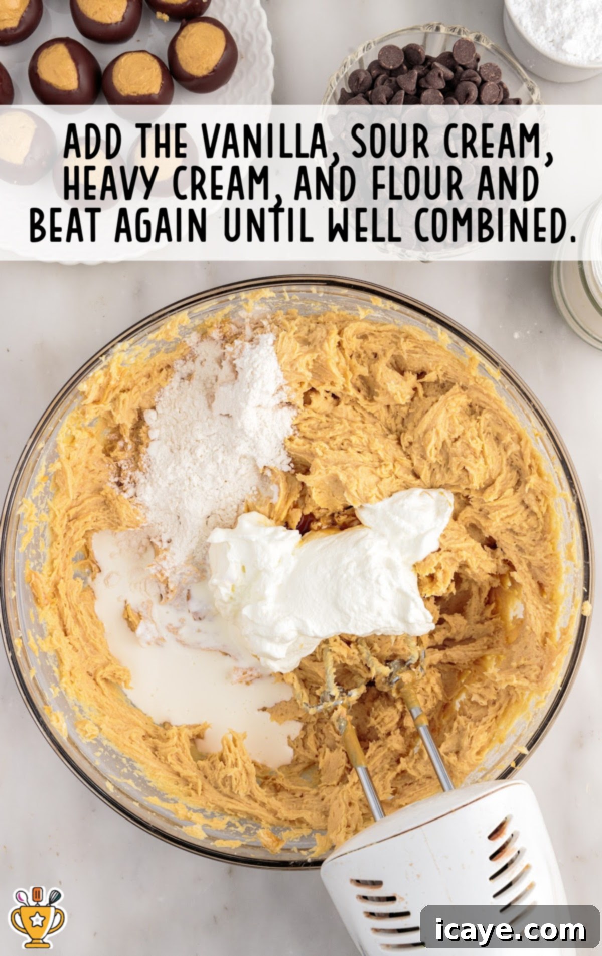 The smooth cheesecake batter in a mixing bowl after vanilla, sour cream, heavy cream, and flour have been added and fully combined, showing a rich, creamy texture ready for eggs.